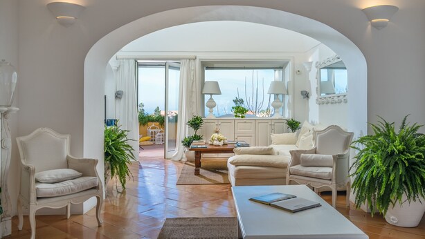 A spacious living area with a large arched doorway leading to an outdoor balcony, furnished with white sofas and armchairs, a coffee table, and potted plants. - Casa Dorotea (Meta)