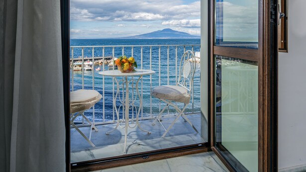 Een balkon met een tafel en twee stoelen, met uitzicht op een waterpartij en een berg in de verte.