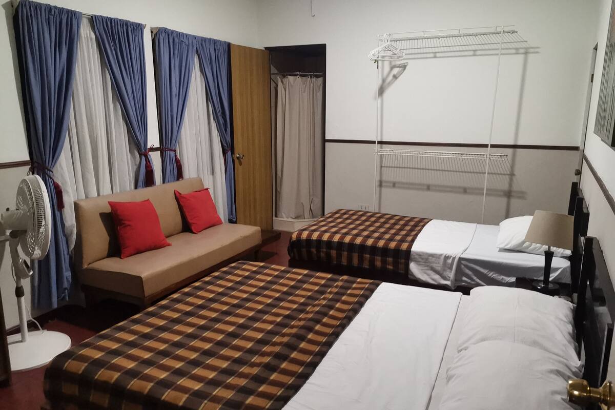 Une chambre d’hôtel avec deux lits, un canapé, un ventilateur et un étendoir.