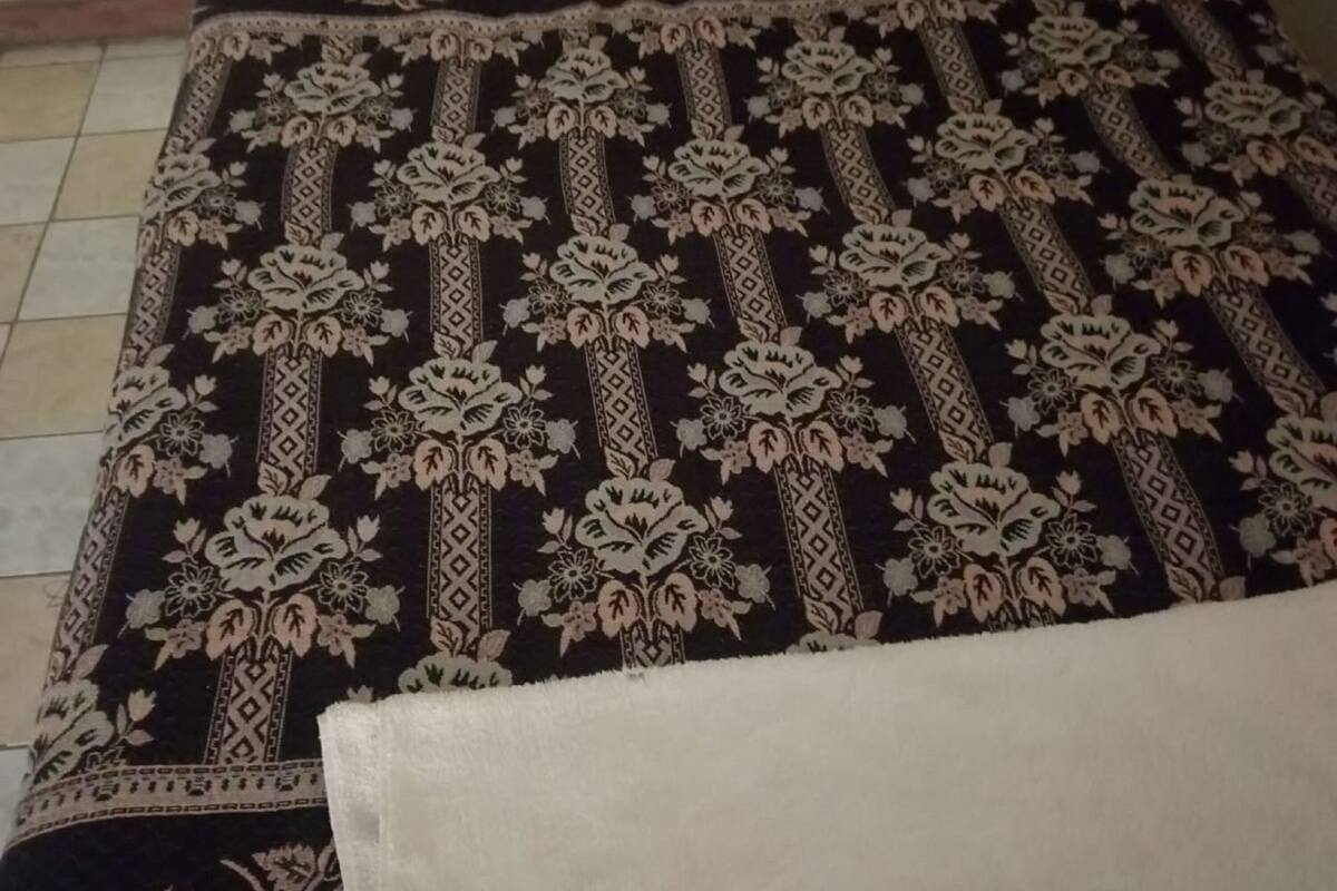 Una cama con una colcha de estampado floral, un almohadón blanco y una manta blanca.