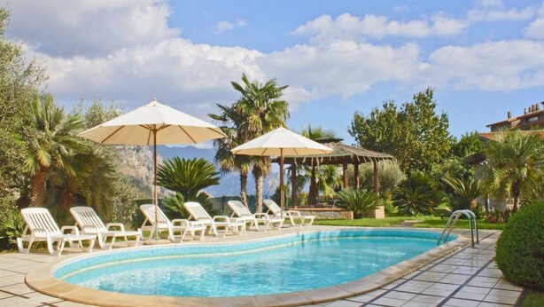 Une piscine entourée de chaises longues et de parasols, bordée de verdure et avec une chaîne de montagnes en toile de fond.
