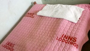 A pink quilted bedspread with the text "INNS LODGINGS" printed on it. - Inns Lodge (Naivasha)