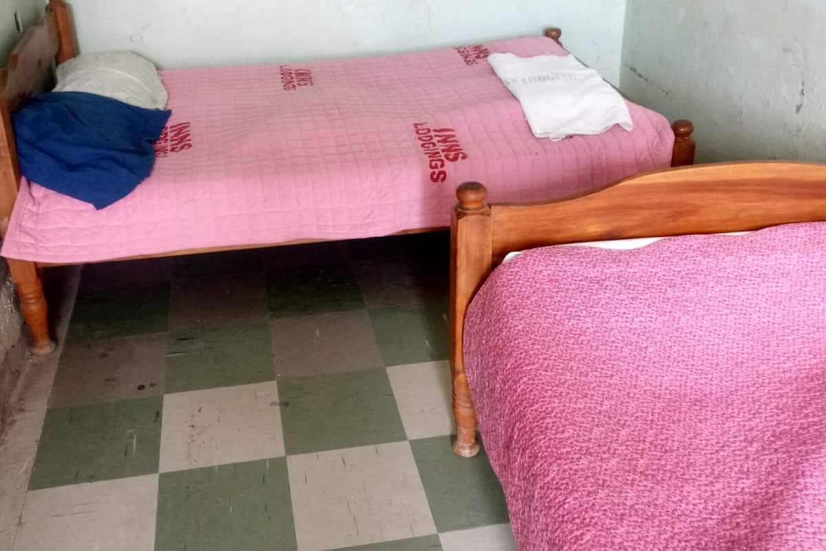 A small room with two beds, one with a pink bedspread and the other with a white bedspread.