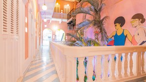 A corridor with a white balustrade, a palm tree, and a mural of two people. - Casa Movida Hostel (Cartagena)