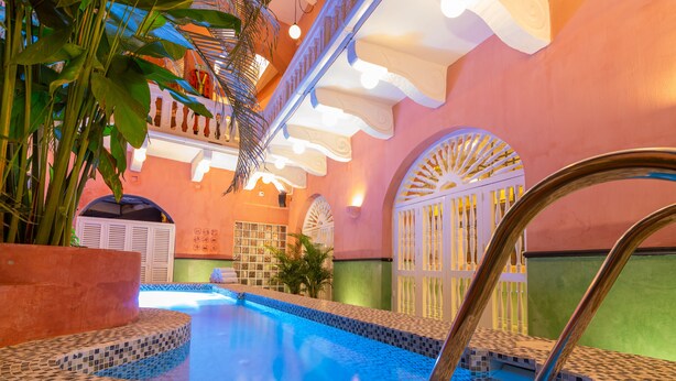 An indoor swimming pool with tiled edges, surrounded by a pink wall with decorative arches and a staircase. - Casa Movida Hostel (Cartagena)