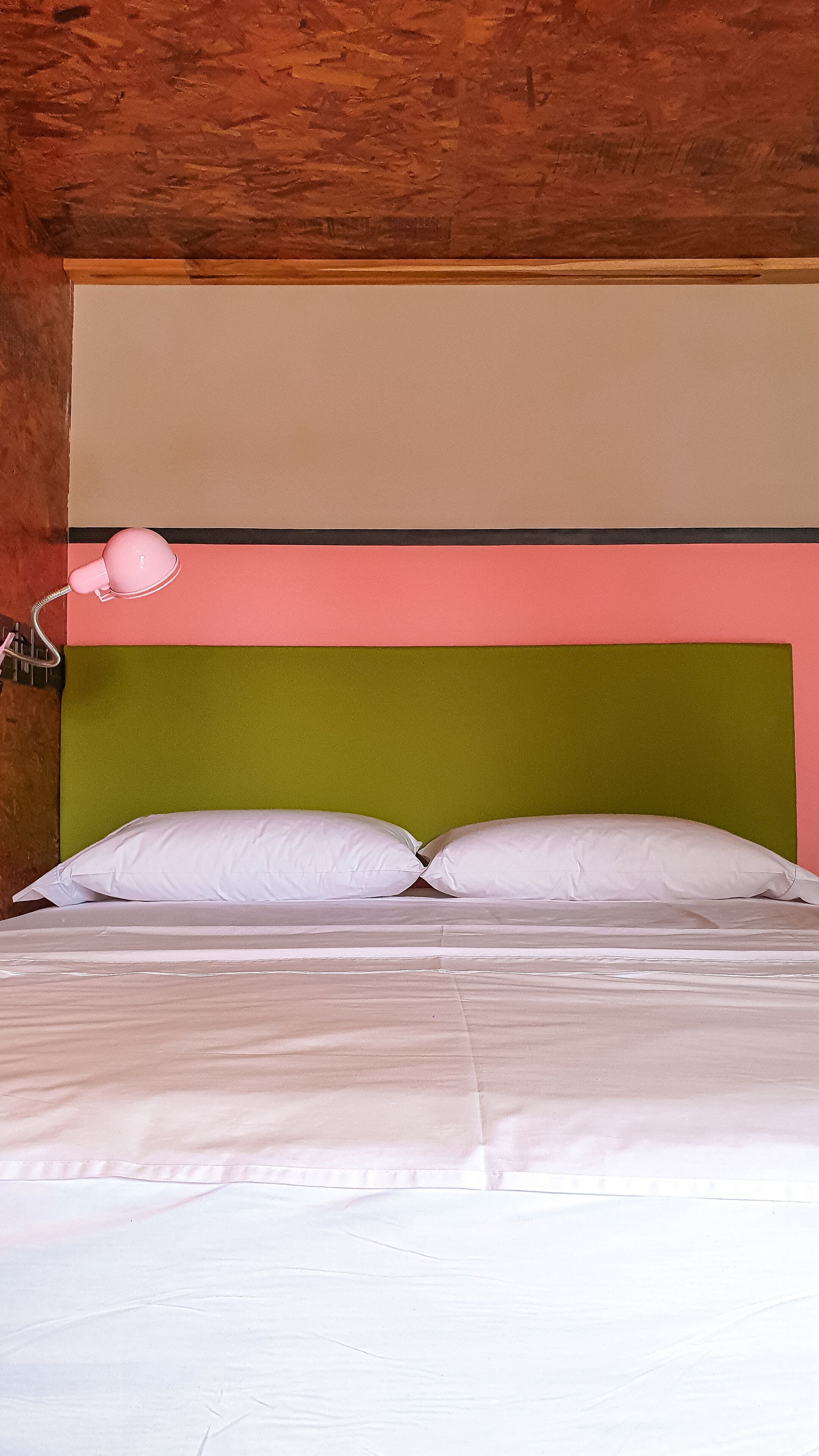 A bed with white linens, a green headboard, and a pink lamp.