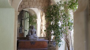 Holvikaarinen kivikäytävä, jossa on Buddha-patsas, ruukkukasveja ja kuvioitu matto.
