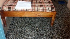 Een enkel bed met een geruit sprei en kussens, een stoel en een blauwe slipper op de vloer.