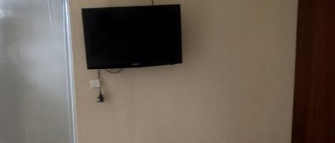 A room with a white table, a chair, a television mounted on the wall, and a door.
