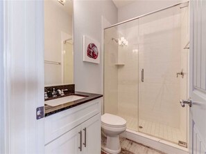 A bathroom with a glass-enclosed shower, a white toilet, and a marble countertop sink. - Sunset Key, 5 Bedrooms, Private Pool, Game Room, Beach, Sleeps 12 (Palm Coast)