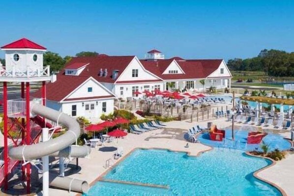 A swimming pool area with a water slide, lounge chairs, and a building with a red roof.