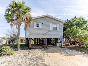 A single-story house with a gabled roof, elevated on stilts, surrounded by sparse vegetation and a dirt driveway. - Pounds Cottage, 1 Bedroom, Ocean Front, Pet Friendly, Sleeps 5 (St. Augustine)