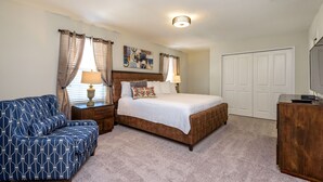 A bedroom with a bed, a blue patterned sofa, a wooden nightstand, a lamp, a painting on the wall, and a closed door. - Private Pool & Spa • Game Room • Waterpark • Golf • Gated • Near Disney (Davenport)