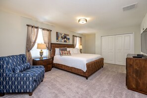 A bedroom with a bed, a blue patterned sofa, a wooden nightstand, a lamp, a painting on the wall, and a closed door. - Private Pool & Spa  • Game Room • Waterpark • Golf • Gated • Near Disney (Davenport)