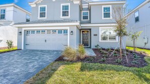 A two-story house with a garage, a front yard with landscaping, and a clear blue sky. - Private Pool & Spa • Game Room • Waterpark • Golf • Gated • Near Disney (Davenport)