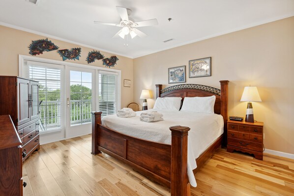 A bedroom with a wooden bed, two bedside tables with lamps, a ceiling fan, and a view through the glass doors.