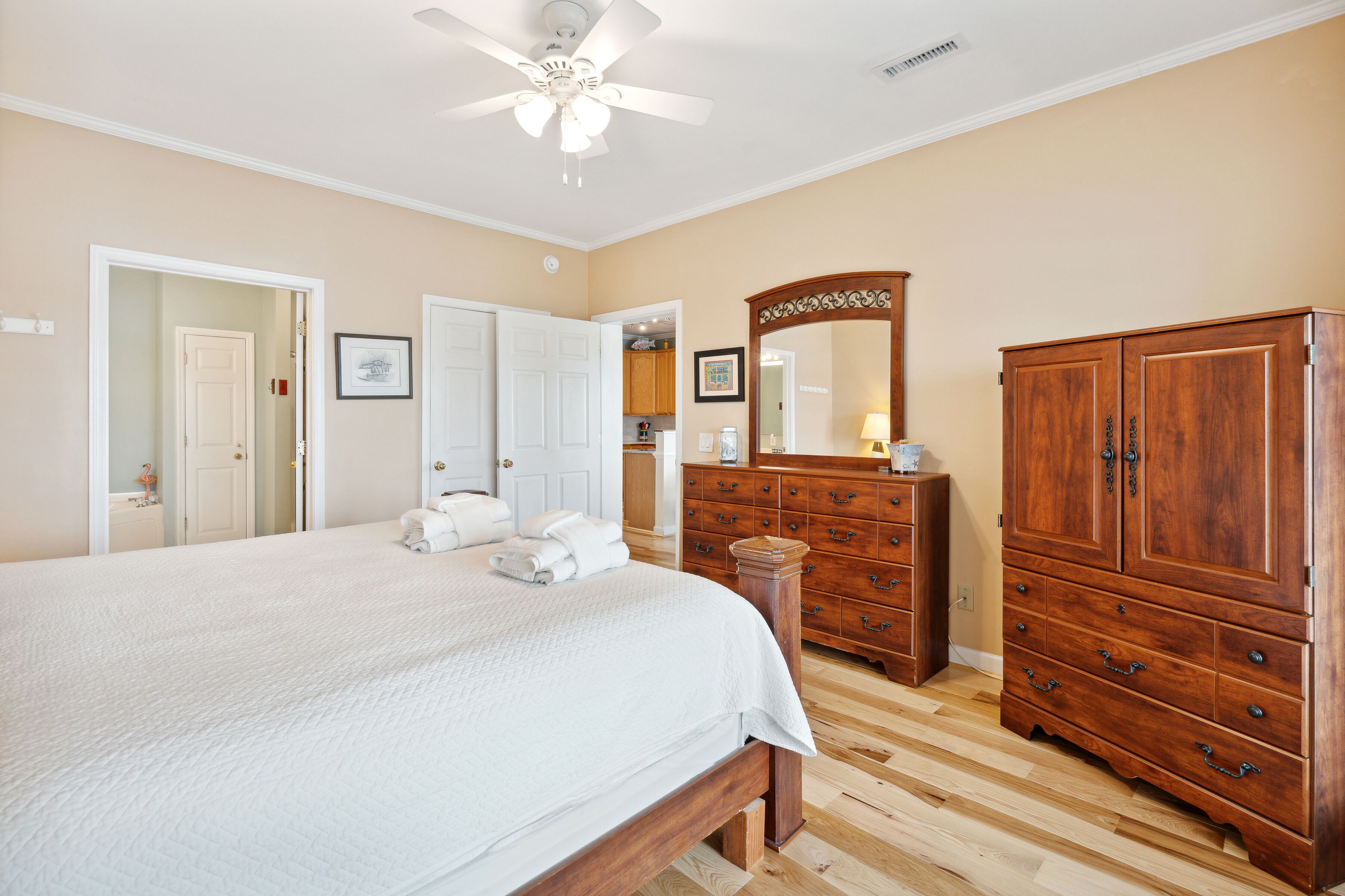 A bedroom with a large bed, wooden dresser, and a ceiling fan.