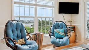 Zwei blaue Korbsessel mit Blick auf Grünfläche, ein Holznachttisch und ein an der Wand befestigter Fernseher.