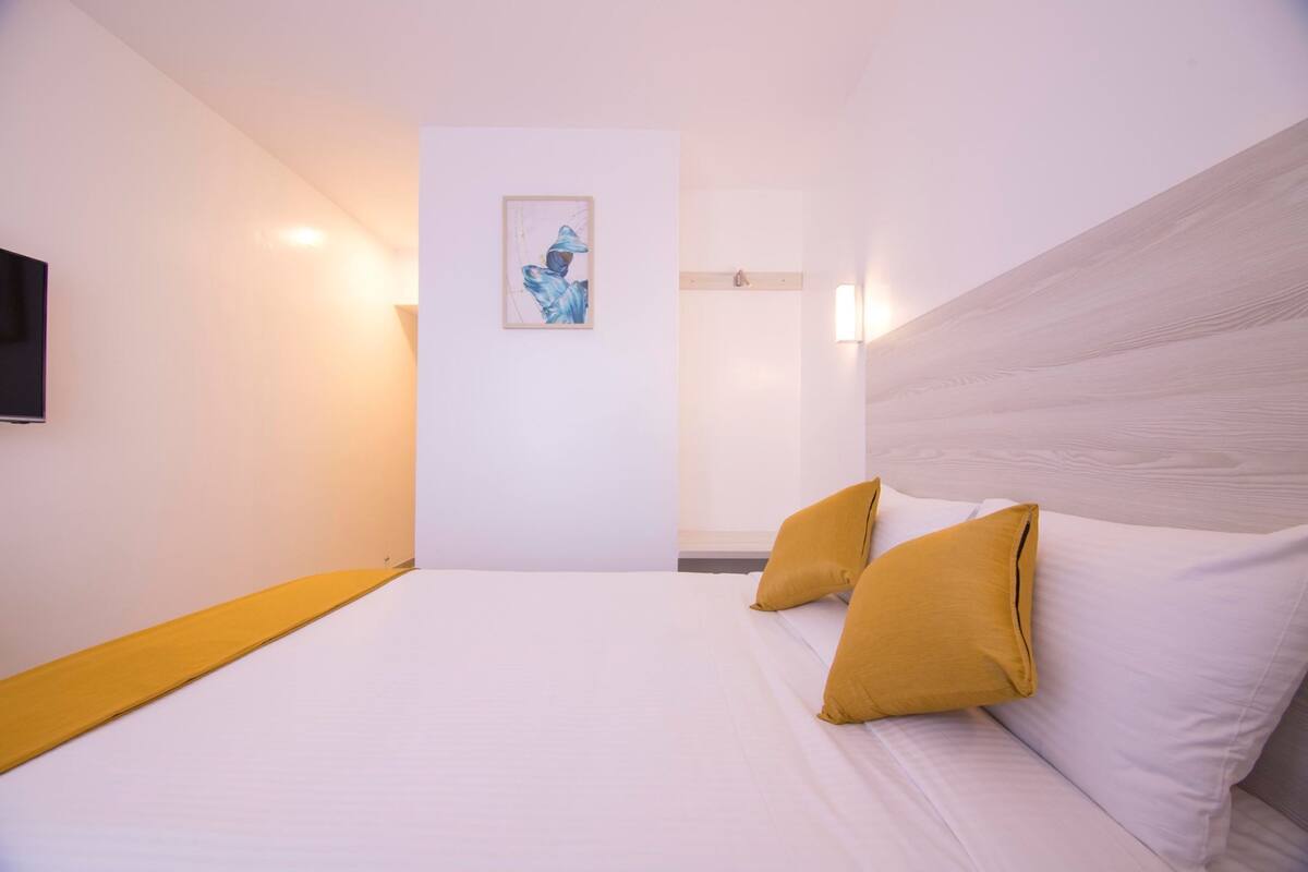 Quarto de hotel com cama, duas almofadas, televisão montada e uma obra de arte emoldurada na parede.