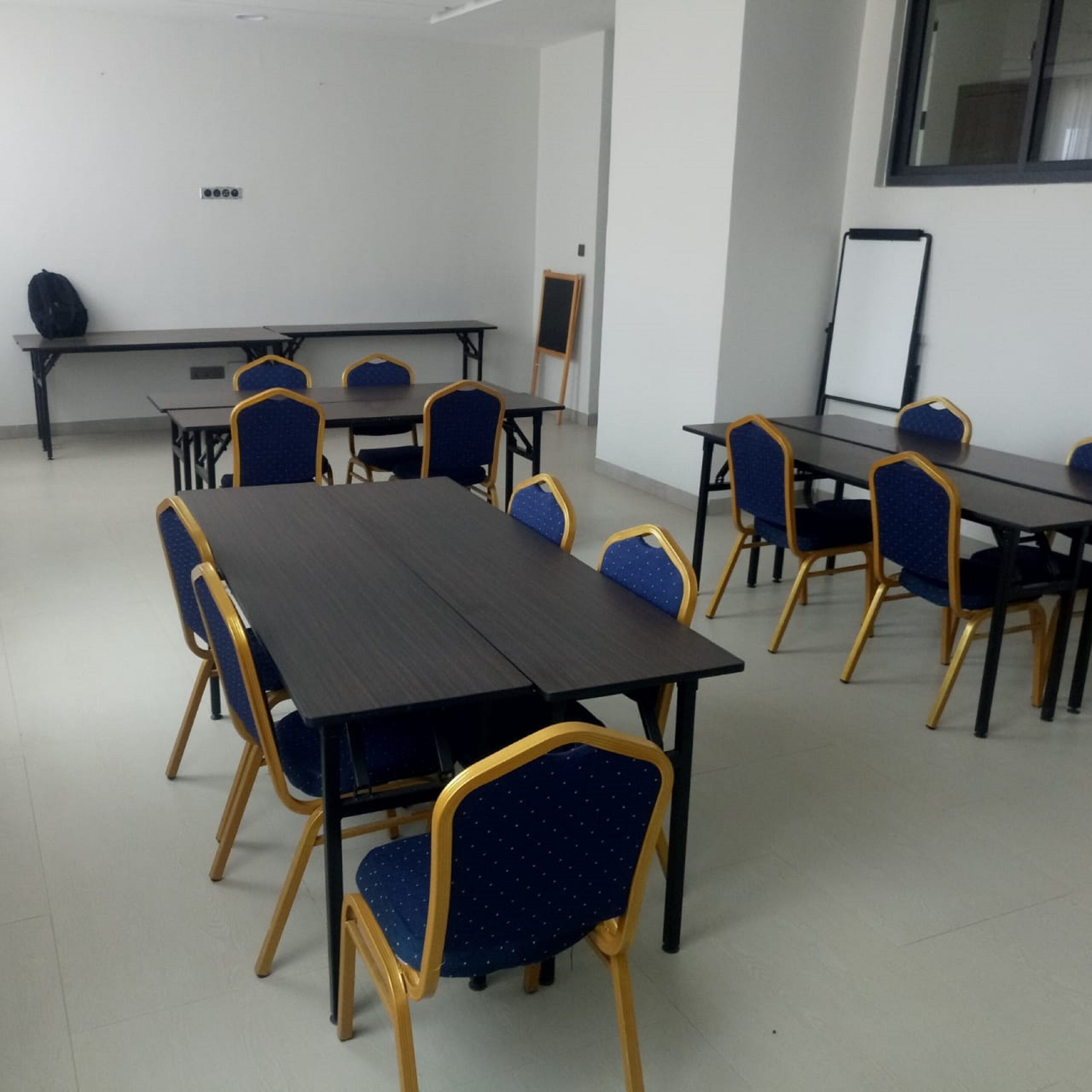 Une salle de conférence équipée d’une grande table, de chaises bleues à armature dorée, d’un tableau blanc et d’un chevalet.