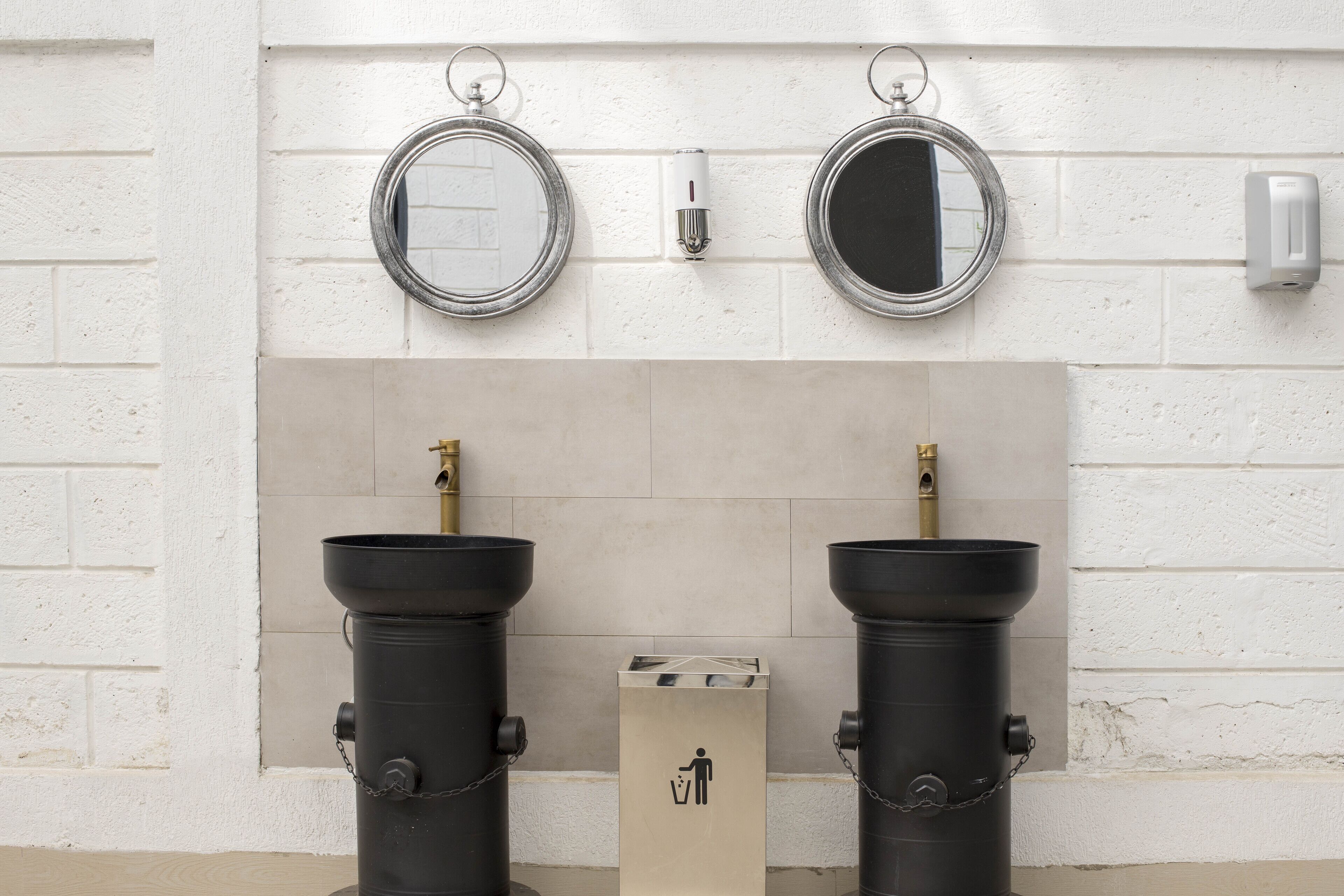 Eine Toilette mit zwei schwarzen Waschbecken, einem Spiegel und einem Mülleimer.