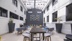 Un espacio interior amplio con una larga mesa y múltiples sillas, rodeado de paredes de ladrillo blanco y ventanas grandes.