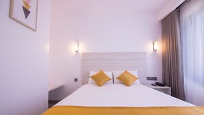 Una habitación de hotel con una cama grande, dos mesitas de noche, una lámpara de noche, un cuadro en la pared y una ventana con cortinas.