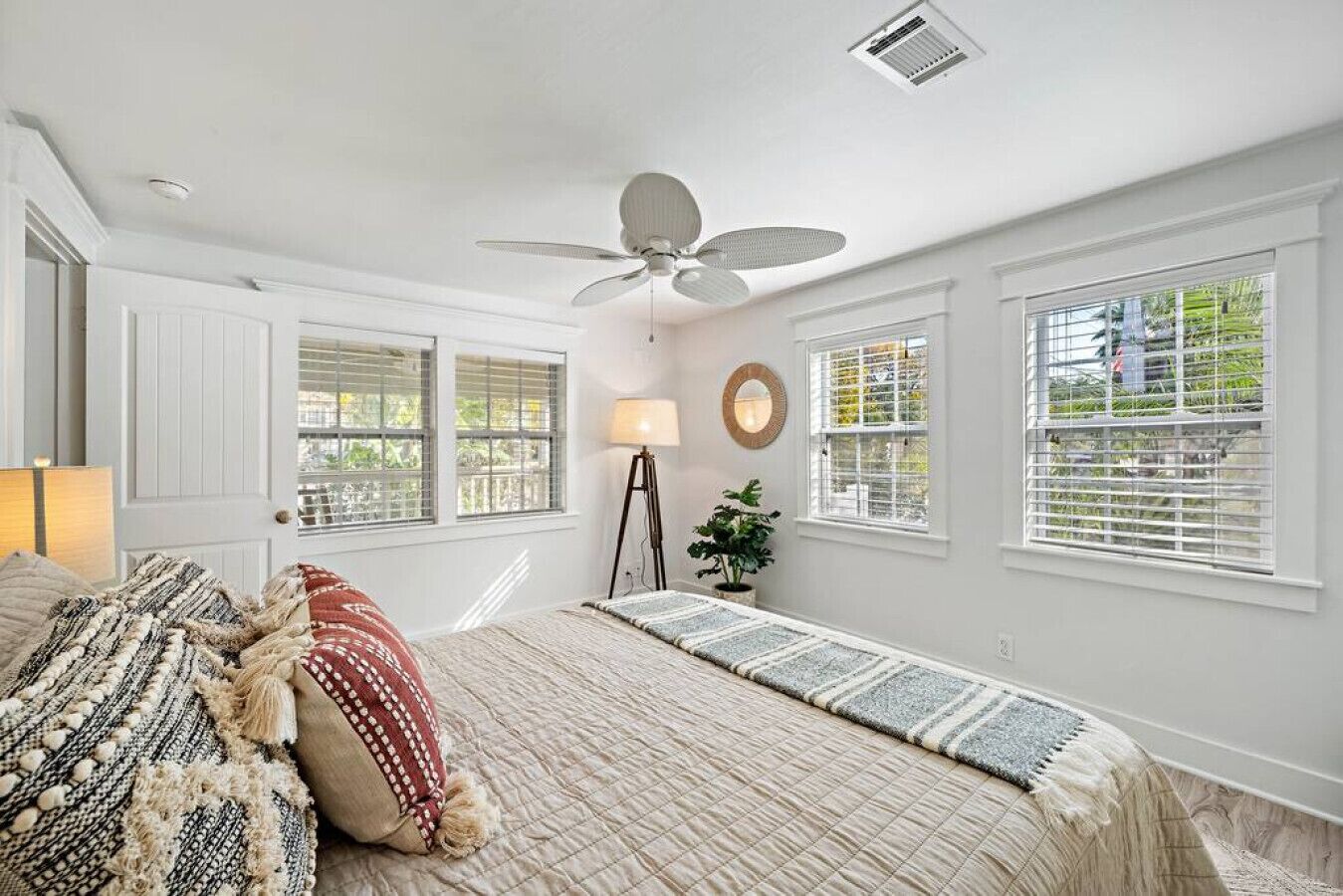 Une chambre à coucher avec un lit, une lampe sur pied, un ventilateur de plafond et des fenêtres équipées de stores.
