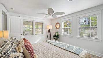 Une chambre à coucher avec un lit, une lampe sur pied, un ventilateur de plafond et des fenêtres équipées de stores.