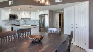 Una cocina moderna con armarios blancos, electrodomésticos de acero inoxidable y una mesa de comedor de madera con sillas.