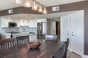 A modern kitchen with white cabinets, stainless steel appliances, and a wooden dining table with chairs.