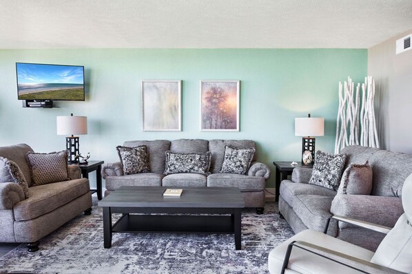 A living room with a sofa set, a coffee table, two wall-mounted lamps, and two framed artworks.