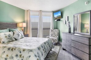 A bedroom with a bed, a chair, a dresser, a TV, and a window with blinds.