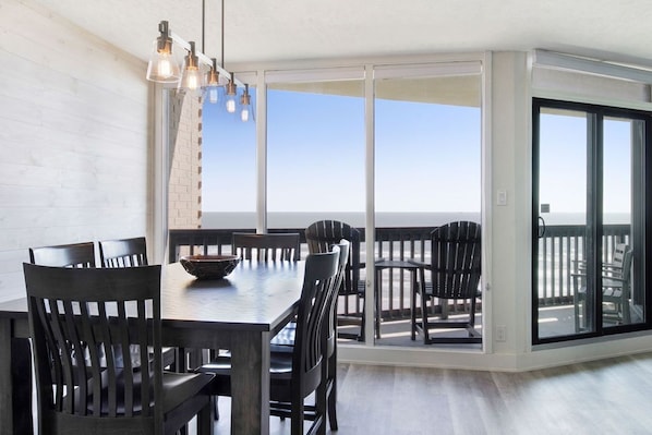 A dining area with a large table and chairs, a bowl on the table, and a view through large glass doors to an outdoor deck.