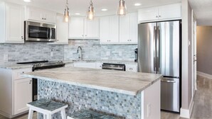 Una cocina moderna con armarios blancos, un refrigerador de acero inoxidable, un microondas integrado y un salpicadero de azulejos.
