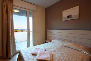 A hotel room with a bed, a nightstand, a painting on the wall, and a view through the door. - Hotel Paradiso Verde (Bibbona)
