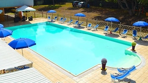 Una piscina rectangular con sillas reclinables y sombrillas azules a su alrededor.