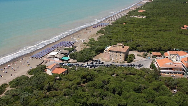 Vista aérea de una zona costera con playa, coches aparcados y edificios.