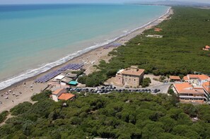 An aerial view of a coastal area with a beach, parked cars, and buildings. - Hotel Paradiso Verde (Bibbona)