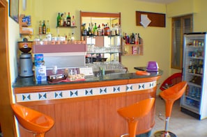 A bar area with a counter, stools, and shelves stocked with bottles and glasses. - Hotel Paradiso Verde (Bibbona)