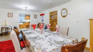 Un coin repas avec une longue table dressée pour le repas, une cuisine en arrière-plan et une porte en bois.