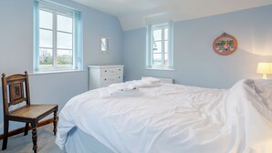 Une chambre à coucher comprenant un lit, deux fenêtres, une commode, une chaise et un élément décoratif mural.