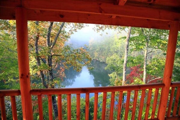 A wooden cabin with a view of a forested area and a lake.