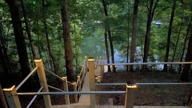 Un escalier en bois, doté de rampes métalliques, mène à une zone boisée.