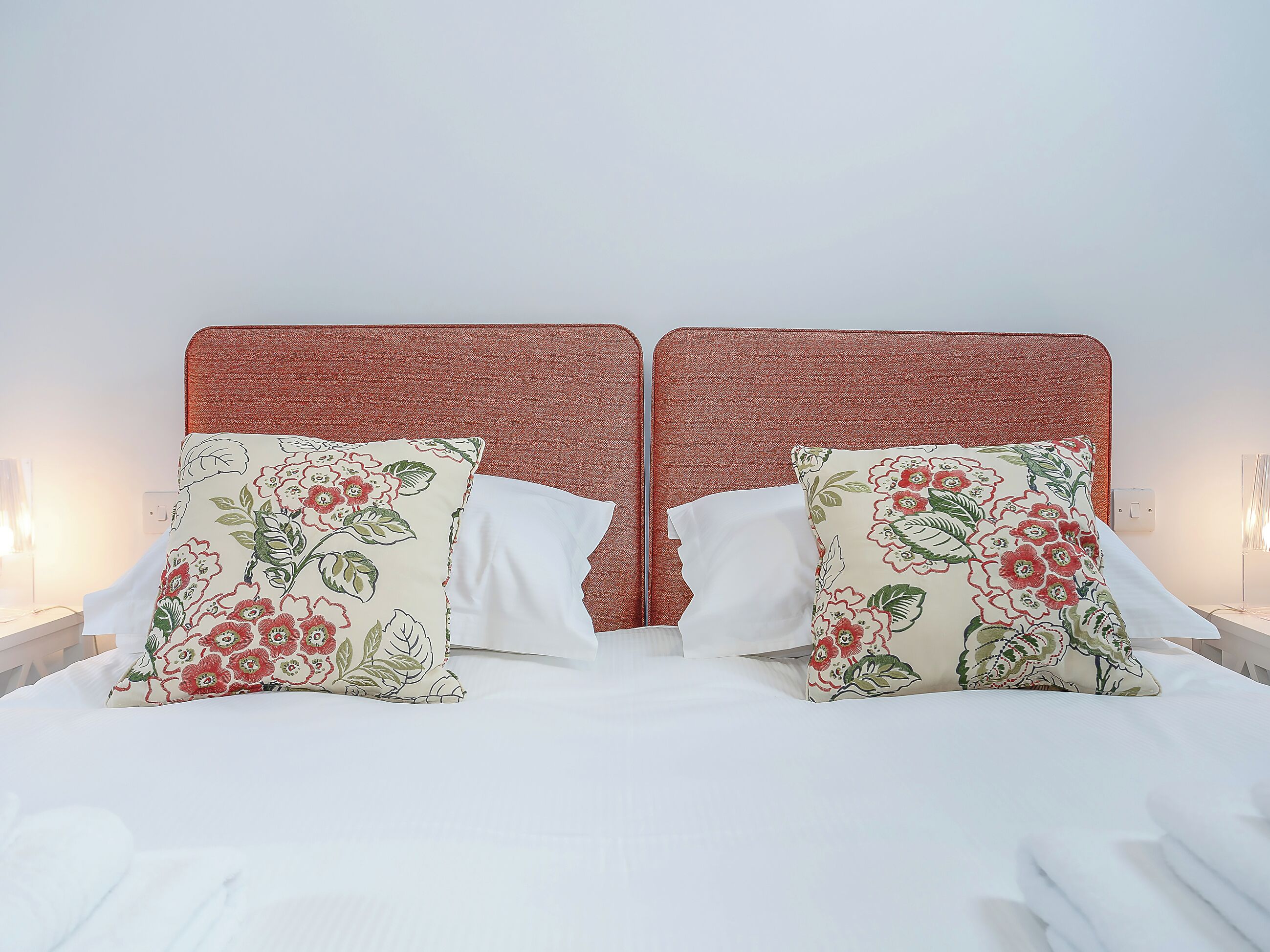 A double bed with floral-patterned pillows and a red headboard.