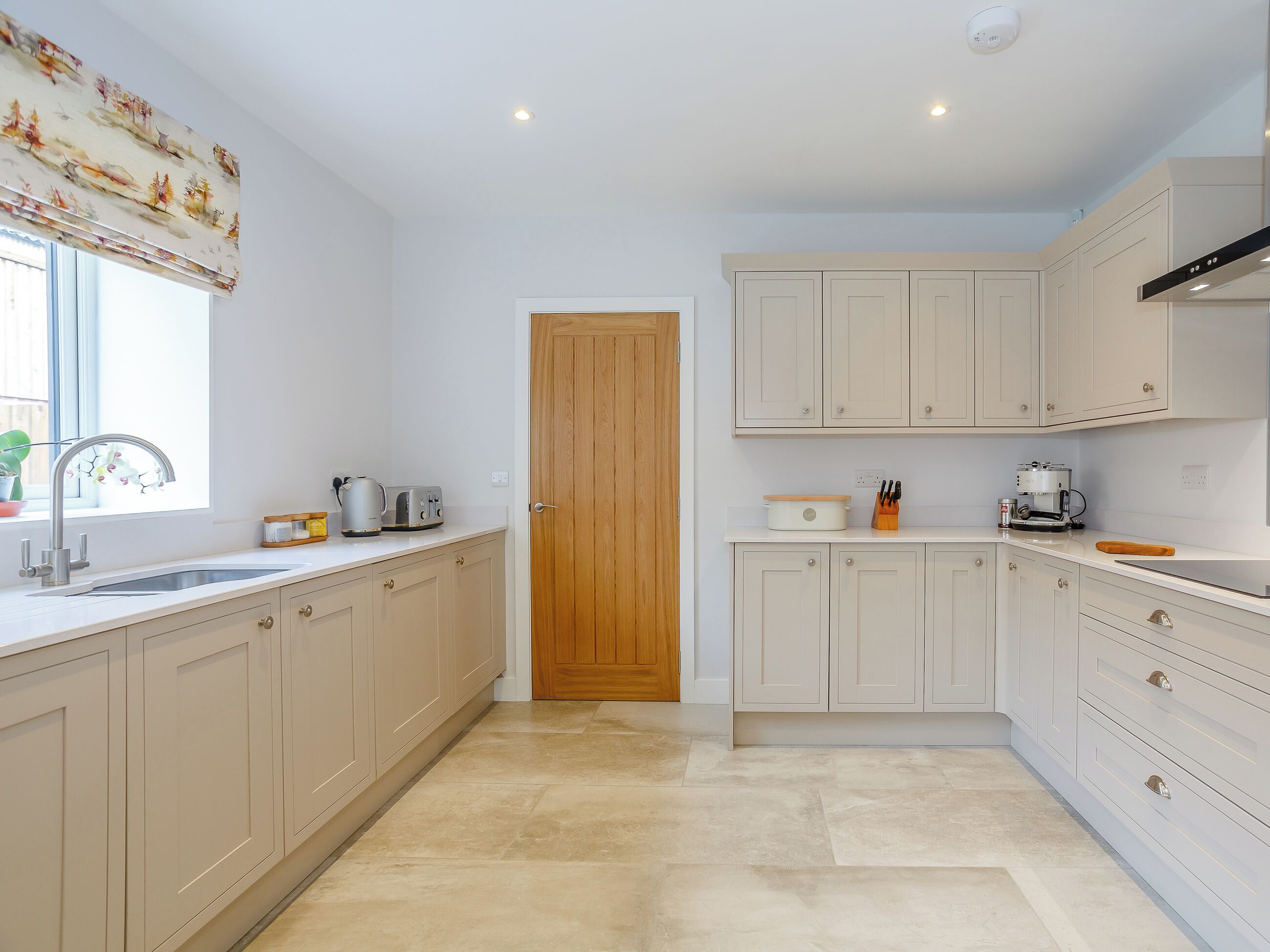 A modern kitchen with light-colored cabinets, a wooden door, and a window with a decorative valance.