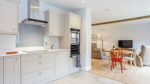 Una cocina moderna con muebles blancos, horno empotrado y una zona de comedor con mesa y sillas.