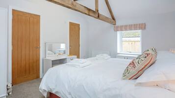 Een slaapkamer met een bed, een nachtkastje met spiegel, een raam met uitzicht op een houten schutting en een zichtbare houten balk aan het plafond.