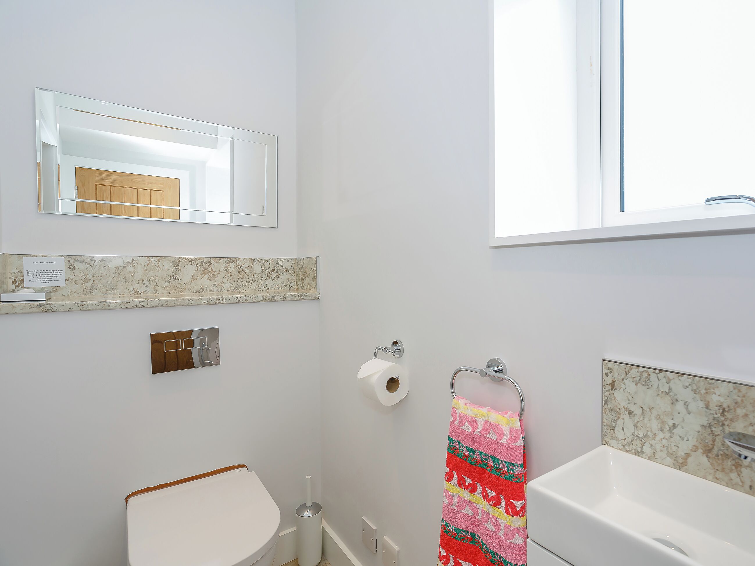 Une salle de bain équipée de toilettes, d’un lavabo, d’un miroir et d’un porte-serviettes.
