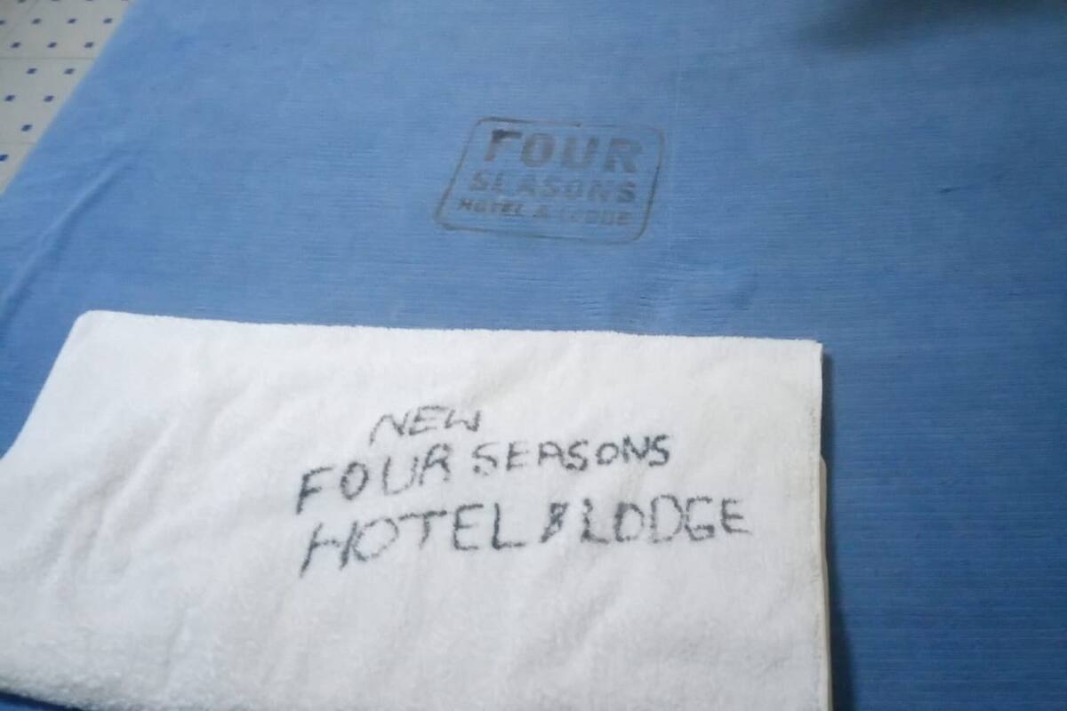 A bed with a blue sheet and a white pillow. A white towel with text is placed on the bed.